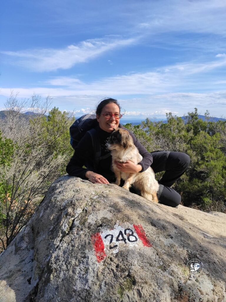 Donna con zaino da trekking e cane su roccia segna percorso