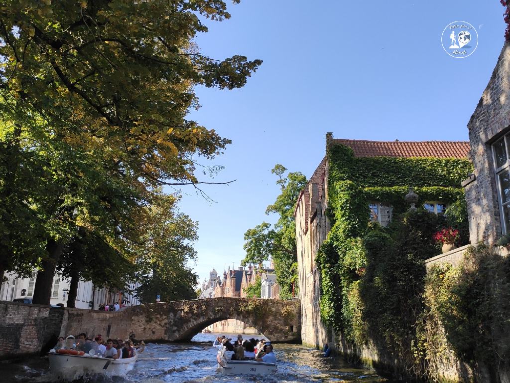 Barche di tuisti sui canali di Bruges. Sullo sfondo un ponte ed edifici tipici